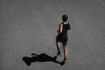 People, sports and achievement. Top shot of athletic dark-skinned runner wearing black sportswear, jogging outdoors, casting shadow upon black pavement, training, preparing for serious marathon