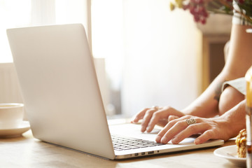 Fototapeta premium Young housewife using computer for shopping online, surfing Internet. Woman typing message on laptop keyboard, communicating with her friends via social networks, sitting at home, enjoying cup of tea
