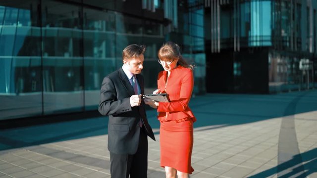 Businesswoman with tablet PC make an offer to customer. Businessman agree, smile and hand shake. 4k medium shot UltraHD. Glass modern building BG. Teal and orange. Successful Deal Concept.