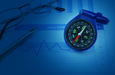 Blue compass with pen and glasses on growth financial chart and