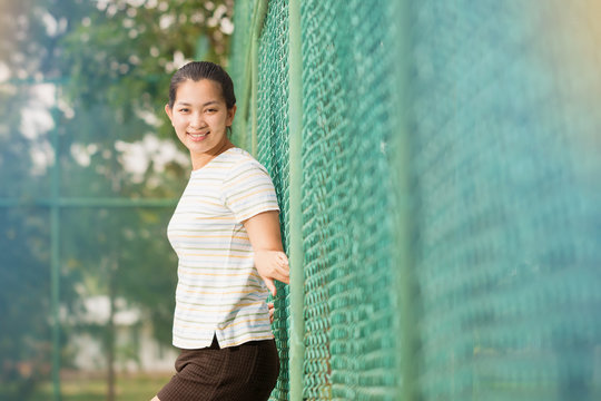 Asian female relax and smile standing on tennis court 