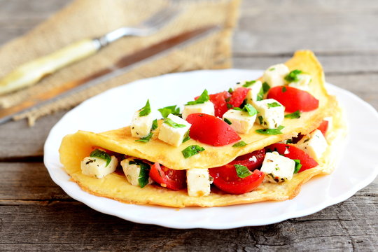 Omelet stuffed with cheese, fresh tomatoes and parsley. Stuffed omelet on a plate and on old wooden background. Eggs recipe. Breakfast menu. Closeup