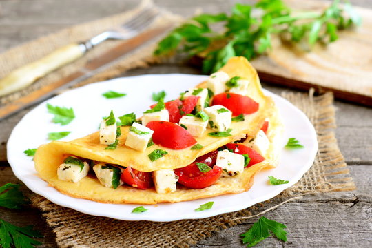 Omelette with cheese, tomatoes and parsley on a plate on old wooden background. Stuffed omelette dish. Vintage style. Closeup