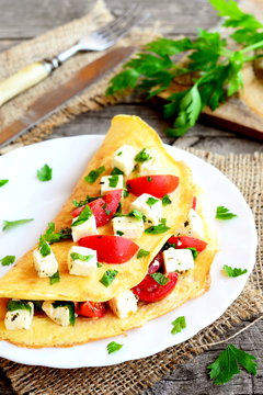 Omelette stuffed with cheese, fresh tomatoes and parsley. Stuffed omelette on a plate and on old wooden background. Eggs breakfast dish. Closeup