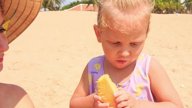Closeup Little Girl with Pigtail Eats Fruit on Sand Beach