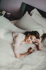 Obraz na płótnie Canvas Portrait of beautiful bride with fashion veil posing on bed at wedding morning. Makeup. Brunette girl with long wavy hair styling. Wedding dress.