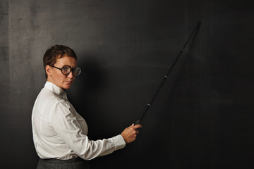 Angry teacher with pointer shows something on black chalk board , stays in left part of image