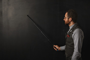 Serious bearded professor in plaid shirt and tweed vest, wearing glasses, shows something on school...