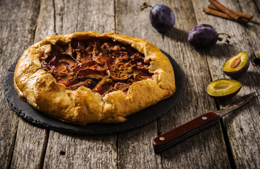 Homemade Rustic Plum Tart with cinnamon, galette on a rough wooden background. Selective focus 