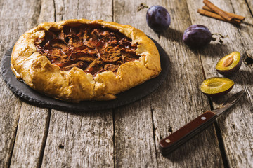 Homemade Rustic Plum Tart with cinnamon, galette on a rough wooden background. Selective focus. Toned 