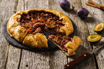 Homemade Rustic Plum Tart with cinnamon, galette on a rough wooden background. Selective focus 