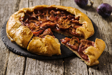 Homemade Rustic Plum Tart with cinnamon, galette on a rough wooden background. Selective focus 