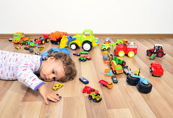 Kid tired after playing with so many toys. Toddler sleeping on the floor, surrounded by lots of cars toys