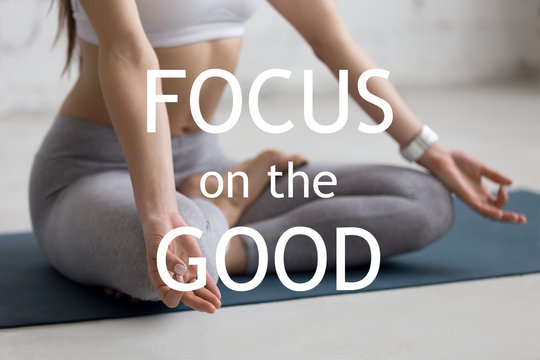 Beautiful young woman working out in loft interior, doing yoga exercise on blue mat, Sitting in Ardha Padmasana, Half Lotus Pose, meditating, close-up. Motivational phrase "Focus on the good"