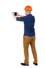 Backview of business man in construction helmet stands and enjoys tablet or using phone. man in a blue shirt and a helmet stands with his back to plate and take pictures.