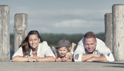 lachende Familie liegt auf Holzsteg am See