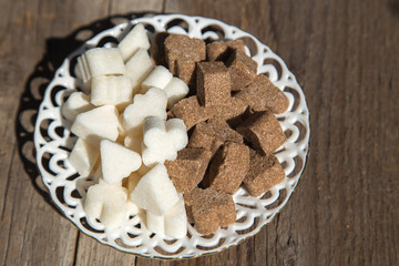 There is a figured brown and white sugar on a porcelain white saucer.There is a saucer on the  wooden surface.