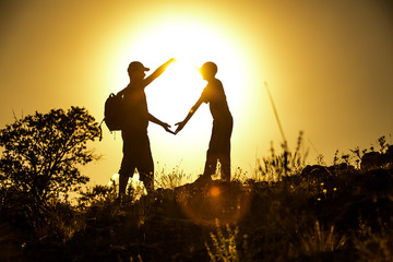 Silhouetted friend forming a heart symbol at golden hour sunset