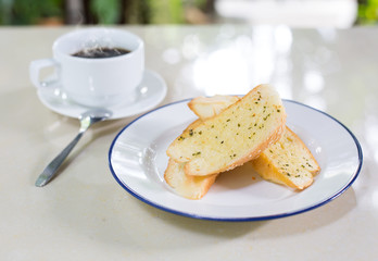 Garlic bread in white dish  with black coffee