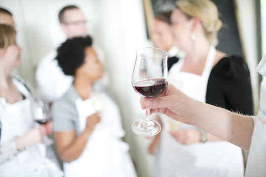 Hand holding red wine, people in background