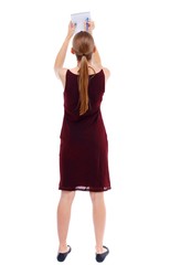 back view of stands woman takes notes in a notebook. girl watching. Isolated over white background. Slim blonde in a burgundy dress writes in a notebook.