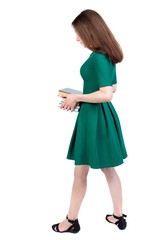 Girl carries a heavy pile of books. back view. slender brunette in a green short dress stands sideways and holds a stack of books.