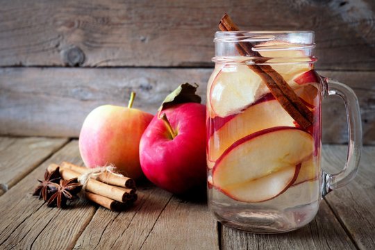 Autumn themed detox water with apple, cinnamon and red pear in a mason jar on a rustic wood background