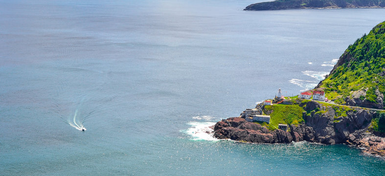 Boats motor past Fort Amherst.  Rugged coastline and Atlantic ocean. Warm summer day in August, speeding boat passes by, appears slow in the vastness.