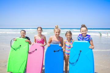 Group of cute kids standing by their boogie boards at the beach while playing in the ocean
