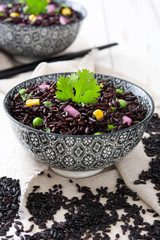 Fototapeta na wymiar Black rice in a bowl and vegetables on white wooden table