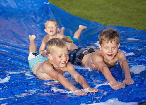 Happy Kids Playing On A Slip And Slide Outdoors