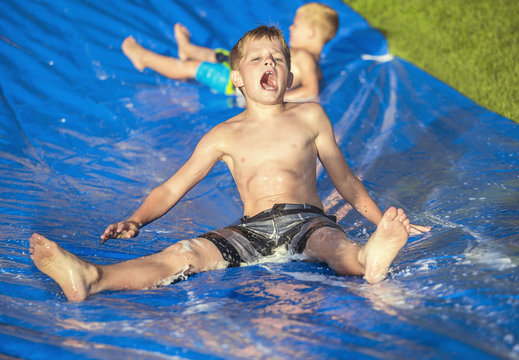 Excited Little Boys Playing On A Slip And Slide Outdoors