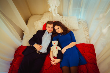 Obraz premium Charming couple lies on red bed holding toy bear on their hands