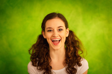 Girl with curly ponytails laughs while standing before light gre