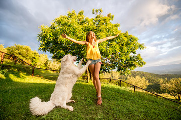Young and happy woman playing with Maremma italian sheepdog on the lawn in the countryside in...