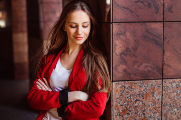 Gorgeous girl leans to the column while posing in red jacket