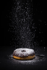 Sprinkling sugar powder on chocolate donut