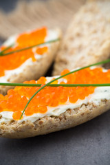 Bread with fresh cream cheese and red caviar on table.