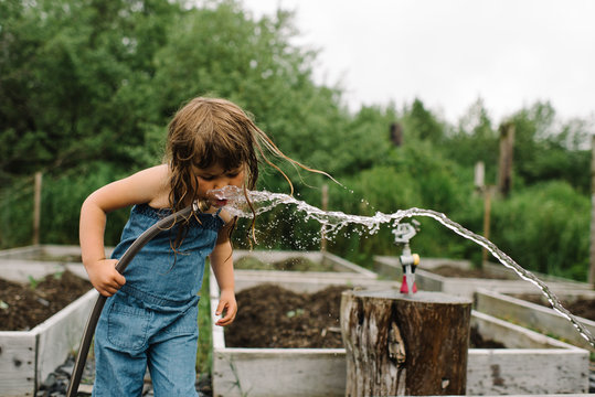 Young girl drinking water from a hose 