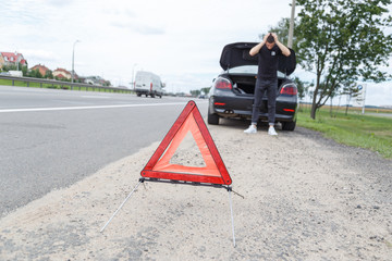 car with a breakdown alongside the road, man sets the warning triangle