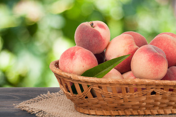 peaches in a wicker basket on wooden table with blurred background