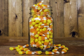 glass jar overflowing with candy corn on rustic wood background