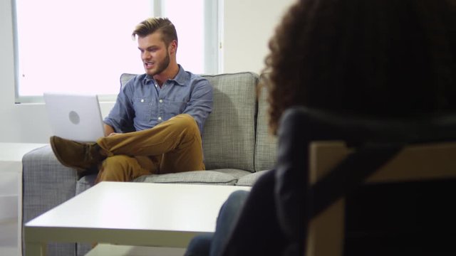 Man talking to woman in living room while using laptop