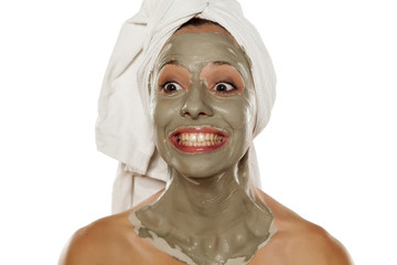 young silly woman with a towel on her head applied a mud mask making funny faces