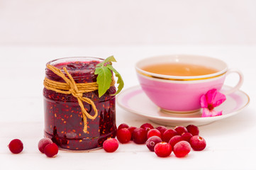 Strawberry jam in a jar, cranberries and a cup of tea