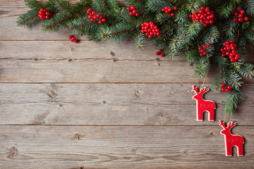 Wooden background with fir branches and red berries, toy reindeer