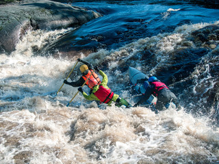 Toned image coordinated team of rowers in helmets and life jackets which sit on the raft, and fighting the rough river against the backdrop water and foam spray