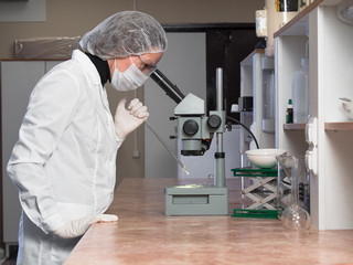 Adult woman protective glasses and medical mask using microscope examines the samples in chemical laboratories against the background of medical equipment for research