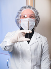 Adult woman closeup protective glasses and medical mask holding in his hand glass syringe with a needle