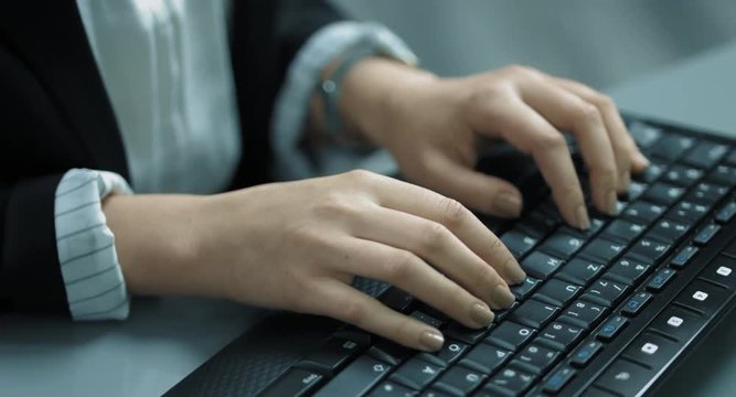 Eine Geschäftsfrau schreibt auf einer Tastatur in einem Büro. Die Tastatur und ihre Hände sind in Nahaufnahme zu sehen. Der Bildstil ist bläulich.